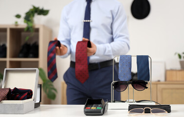 Stand with men's neckties, sunglasses and payment terminal on counter in boutique, closeup