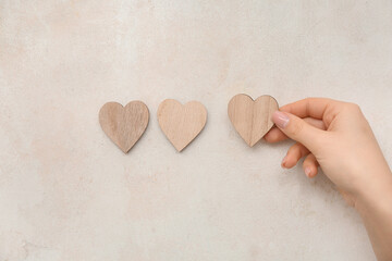 Obraz premium Woman hand placing wooden heart shapes on neutral pastel background, minimalist love concept with copy space, top view