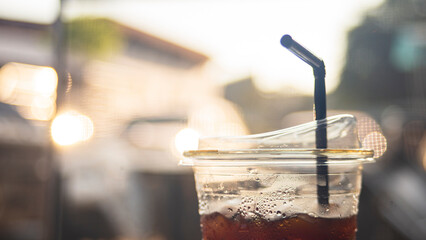Iced coffee in plastic cup with straw on blurred background.