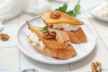 Plate of pear bruschetta with ricotta cheese and walnuts on white tile background