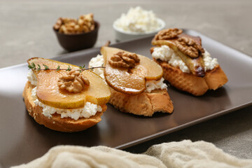 Plate of pear bruschetta with ricotta cheese and walnuts on grey background, closeup