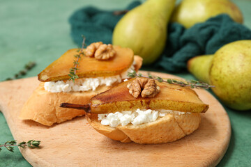 Wooden board of pear bruschetta with ricotta cheese, walnuts and thyme on green background, closeup