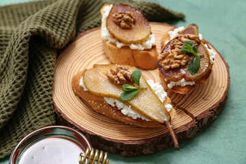 Wooden board of pear bruschetta with ricotta cheese, walnuts and bowl of honey on green background