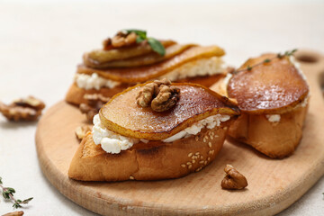 Wooden board of pear bruschetta with ricotta cheese and walnuts on white background, closeup
