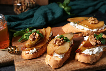 Wooden board of pear bruschetta with ricotta cheese, walnuts and mint on table, closeup