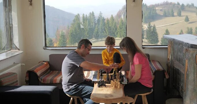 Little boy referees chess game between his parents in a rustic mountain cottage