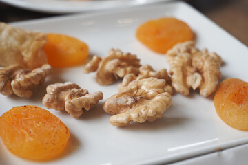 Dried apricots and walnuts on a white plate with a rustic background