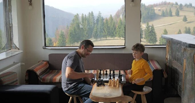 Father and kid play chess in a rustic mountain chalet