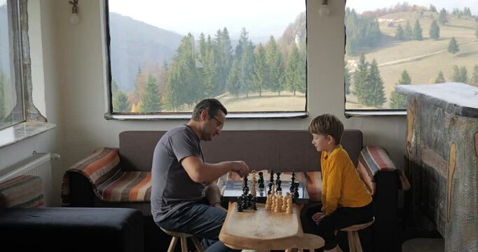 Boy and dad play chess in a rustic mountain chalet