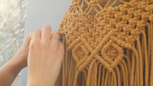 Crafting at home, macrame knitting. A woman's hands weave a decorative pattern using thick yellow cotton cords. Handmade creation of wall art from rope. Artistic handicraft and textile design