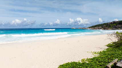 White sandy beach touched by turquoise ocean waves under a clear sky. La Digue, Seychelles. Grand Anse Beach.