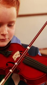 Cute pupil playing violin in classroom