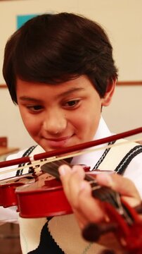 Cute pupil playing violin in classroom