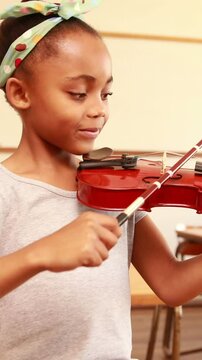 Cute pupil playing violin in classroom