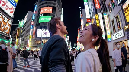 Wide-angle shot of a bustling city street at night, capturing vibrant neon signs and people walking, reminiscent of a travel video scene.