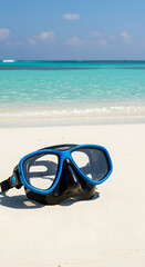 Blue diving mask lies on a white sand beach with turquoise water in the background, inviting to snorkeling and exploring underwater world.