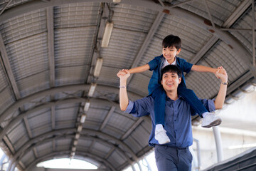 Young Asian father holds his son around his neck enjoy walking around the city.