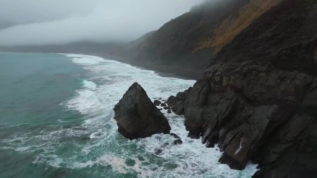 Rugged dramatic untouched coastline surf waves crashing boulder rocks USAL Beach campground cloud layer mist rain fog aerial drone California PNW Lost Coast Trail morning nature landscape backwards