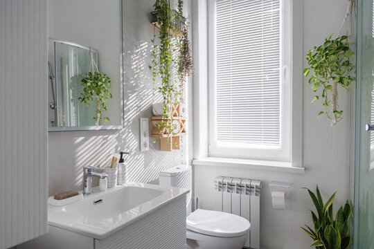 Stylish clean white bathroom with light gray tiles on the walls and lots of indoor plants.