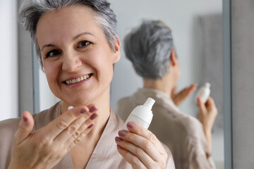 An elderly woman in her age, takes care of her mature skin using a cream against wrinkles