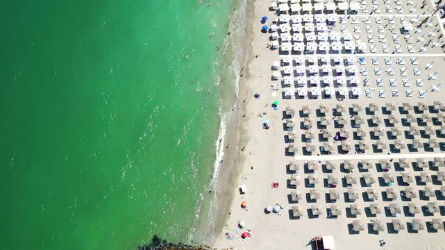 Eforie Nord Beach, Romania, aerial perspective. Famous travel destination. Season time, beach full with sunshades. People at the beaches. Turquoise water. Camera in tilt down. Drone going forward.