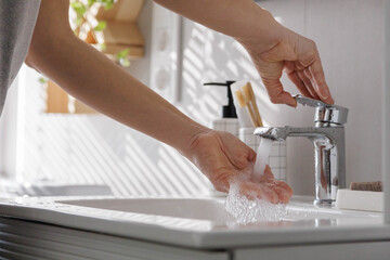 A woman opens clean running water in the faucet to wash and disinfect her hands.