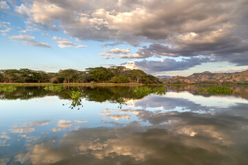 Lake Suchitlán in Suchitoto, El Salvador, creates a mirror reflection of dramatic clouds, trees, and rolling hills. A stunning scene ideal for nature, travel, and landscape photography themes.