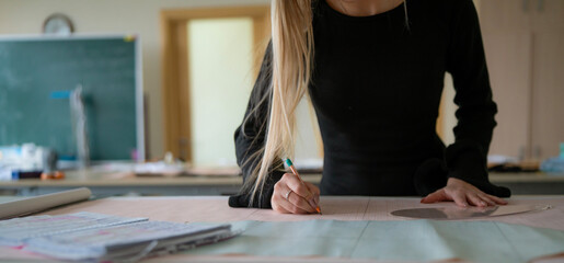 A designer skillfully draws a new textile pattern on paper while surrounded by project materials in a well-lit studio.