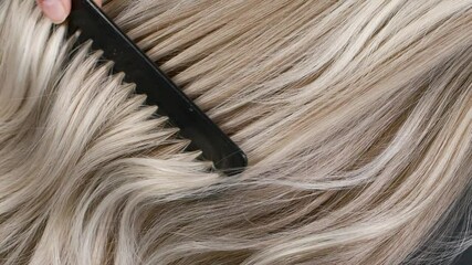 Closeup blond hair texture, slow motion of female hand combing long curly hair
