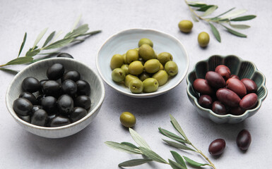 Black, green and kalamata olives with olive branches in bowls on marble