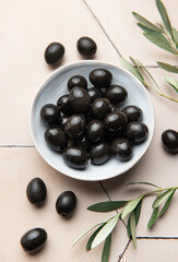 Black olives served in ceramic bowl on hexagonal beige tiles, decorated with olive tree branch