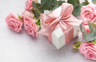 White gift box with pink bow surrounded by pink roses and eucalyptus