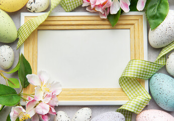 Easter eggs and spring flowers framing empty photo frame on gray background