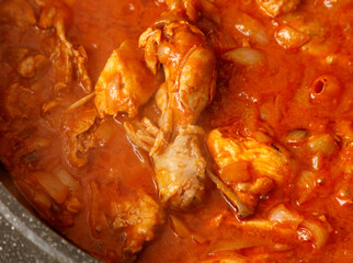 A pot of red sauce with chicken in it