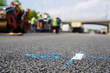 Detailed Close-up of asphalt surface with road markings, with construction workers and equipment blurred in the background, highlighting the quality of the roadwork and paving process.
