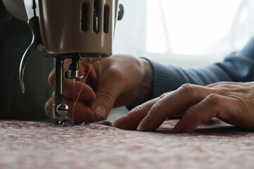 Close-up of women's hands stitching fabric with a needle behind a sewing machine.