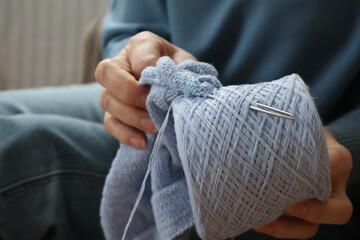 Women's hands hold a spool of blue yarn with knitting needles