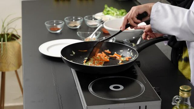Chef is stirring the vegetables in a black frying pan above a double induction Cooker