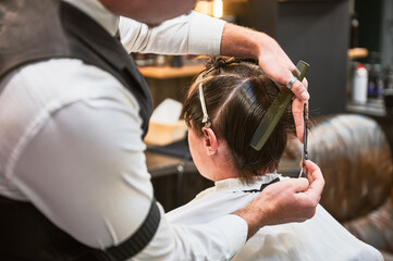 Back view of barber in fancy outfit cutting wet hair. Young client getting stylish haircut. Getting...