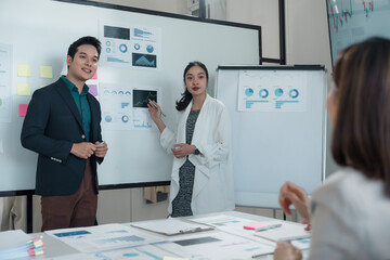 Businesswoman using pen and pointing at whiteboard, presenting charts and statistics to colleagues...