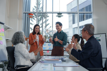 Diverse colleagues showing thumbs up gesture, expressing satisfaction and teamwork during a meeting in a bright, modern office space, celebrating achievement and positive results
