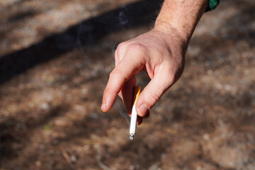 hand of a person, holds a cigar in the park, close-up on brown ground background