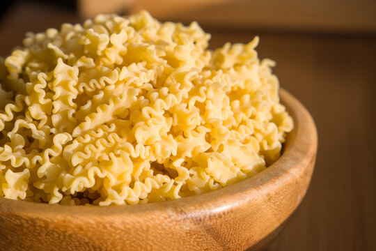 Raw macaroni in a wooden bowl on a wooden table. Close up of a raw italian pasta mafalda. Selective focus.