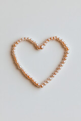 Pearl necklace forming heart shape on white background