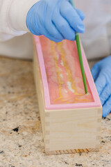 Woman creating decorative swirls in handmade soap using a chopstick.
