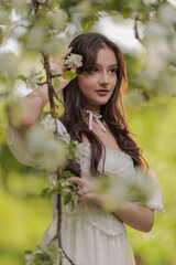 Fototapeta premium Beautiful Girl with long hair poses near white blossoming apple trees