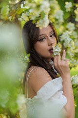 Beautiful Girl with long hair poses near white blossoming apple trees