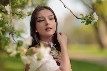 Beautiful Girl with long hair poses near white blossoming apple trees