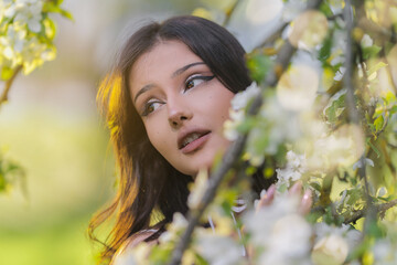 Naklejka premium Beautiful Girl with long hair poses near white blossoming apple trees