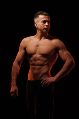 Fototapeta premium Adult male athlete bodybuilder posing on a orange light